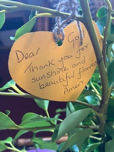 A paper leaf tied to a branch with a handwritten prayer: Dear God, thank you for sunshine and beautiful flowers. Amen.